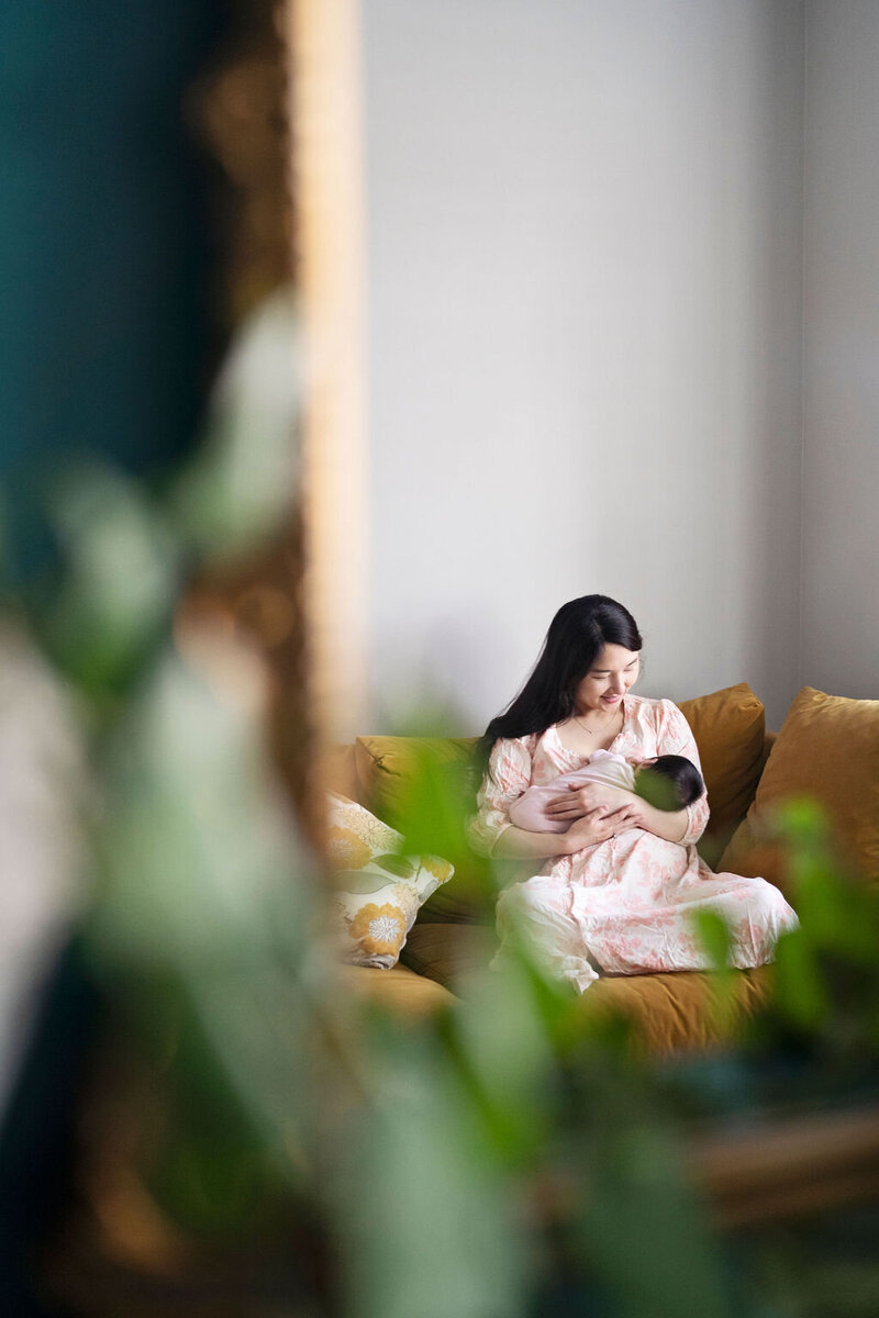 A reflection in a mirror of new mother breastfeeds her baby as she sits on a sofa.