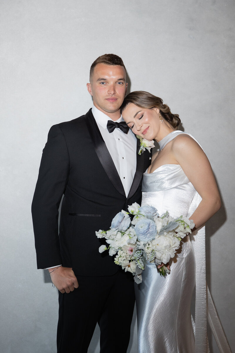 Rhode Island Wedding Photographers | Kelsey Sheehan Photography Timeless Rhode Island Weddings | A couple in formal attire poses for a wedding photo. The woman in a shimmering gown holds a bouquet and rests her head on the man's shoulder, exuding romance.