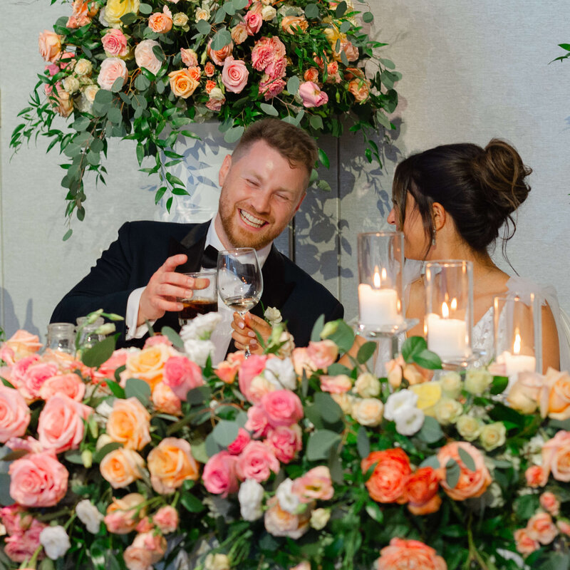 a smiling group clinks glasses with his bride during their Chateau le Parc reception.  Captured by Ottawa wedding photographer JEMMAN Photography