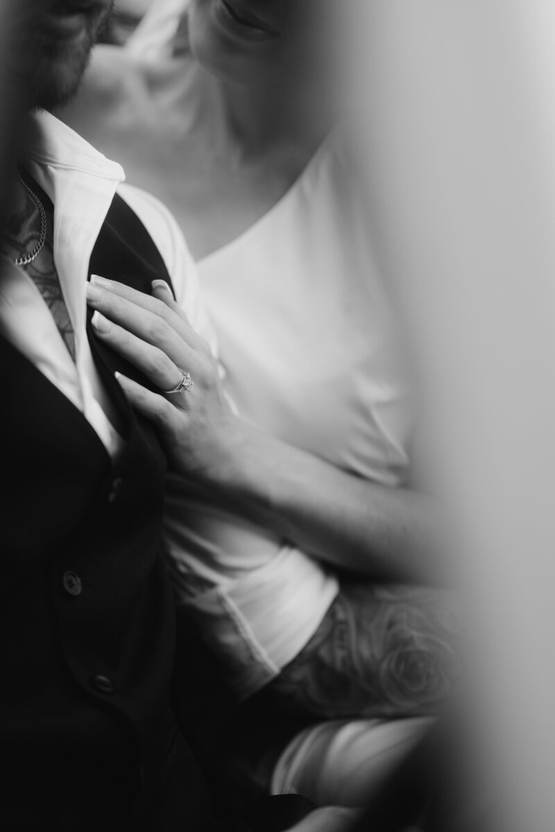 black and white photo of brides hand with engagement ring resting on grooms chest