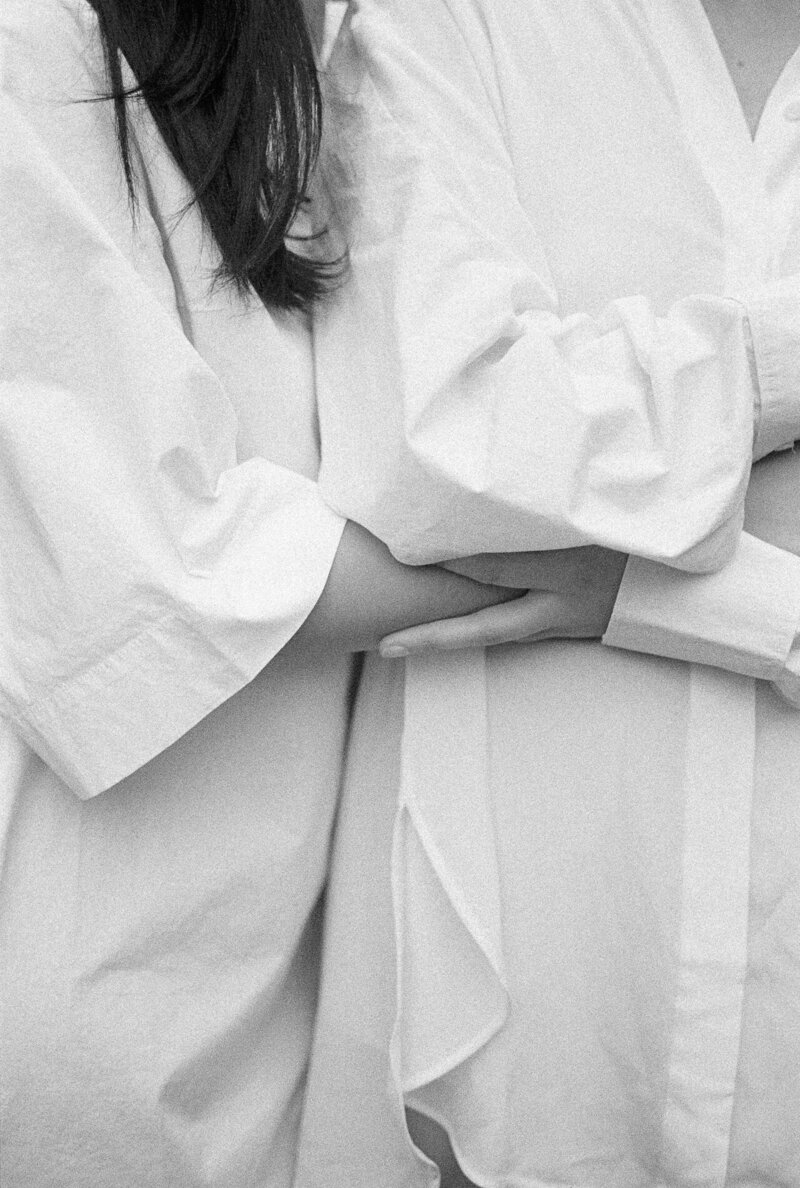 Black and white photo of two people in white shirts holding each other closely, with hands gently placed on each other's backs, capturing a sense of intimacy and comfort.
