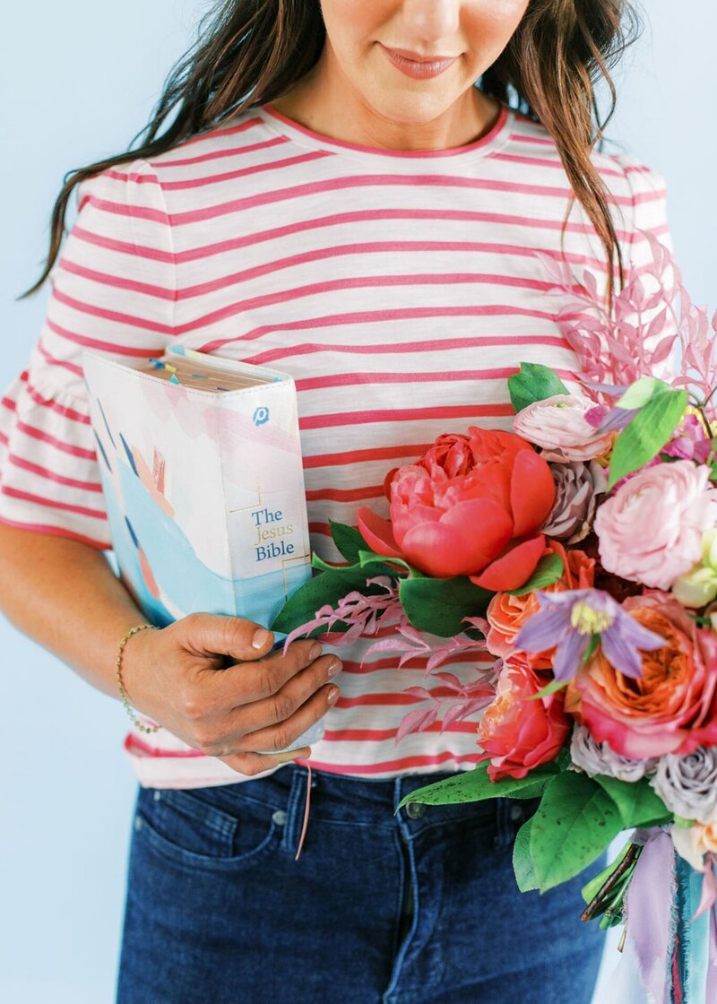 Woman holding colorful bouquet of peonies, roses, and ranunculus with a book in hand.