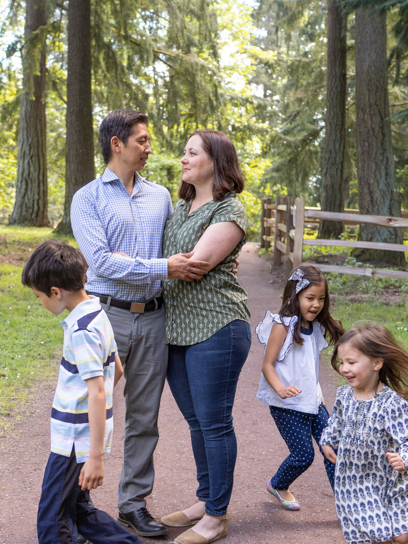 three children are running around circling their parents who are embracing in the middle.