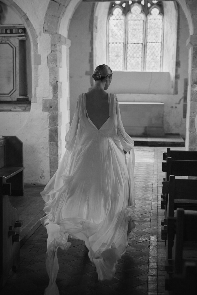 Backless silk flowing wedding dress on bride walking down aisle
