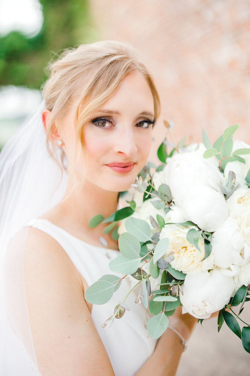 alabama bride smiling into camera while holding white flowers to her face