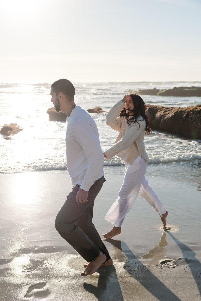 Couple running hand in hand on a beach in La Jolla.