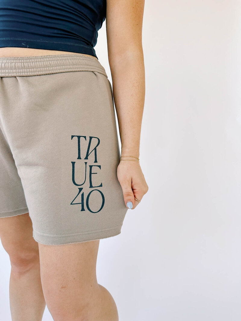 Close up on tan sweat shorts with navy True40 logo on them