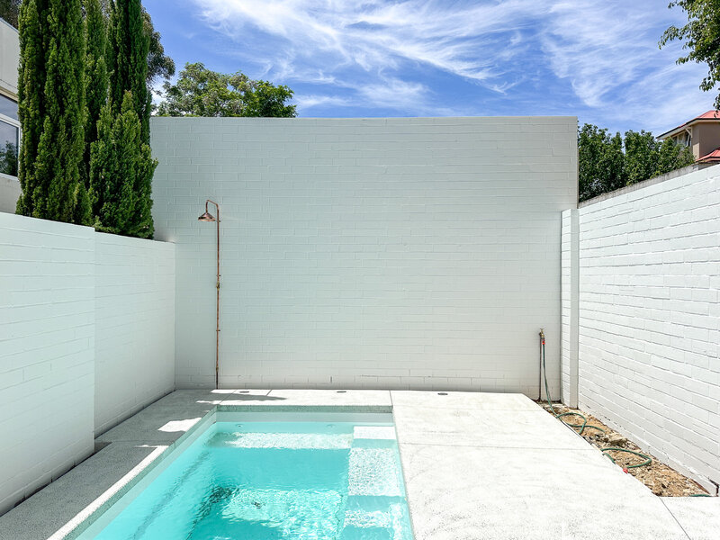 White brick walls surrounding bright blue pool and copper shower in the corner