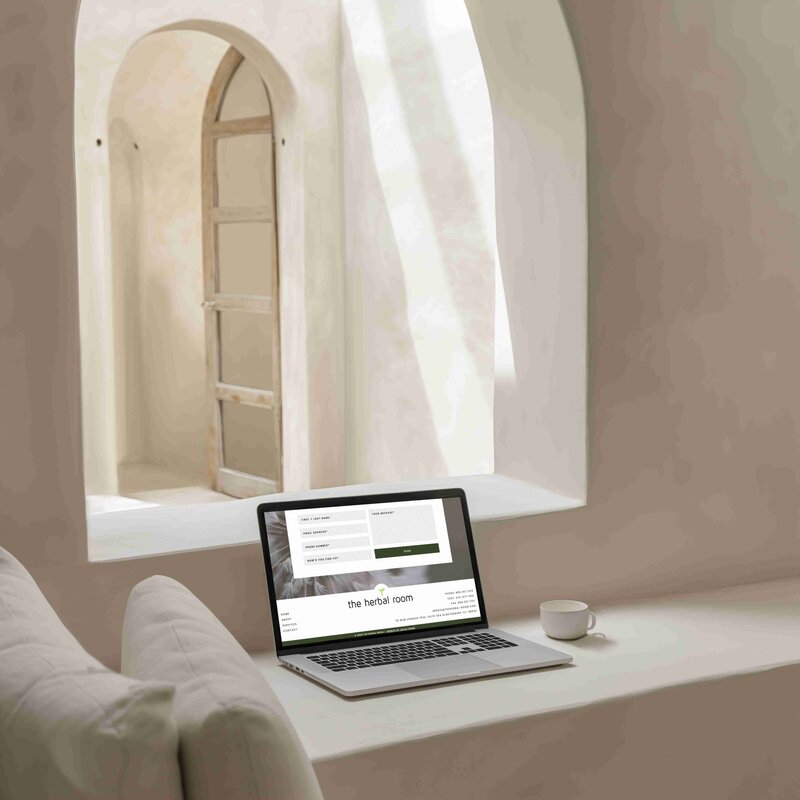 A laptop on a window sill, overlooking a bright white room, with a holistic website design on display.