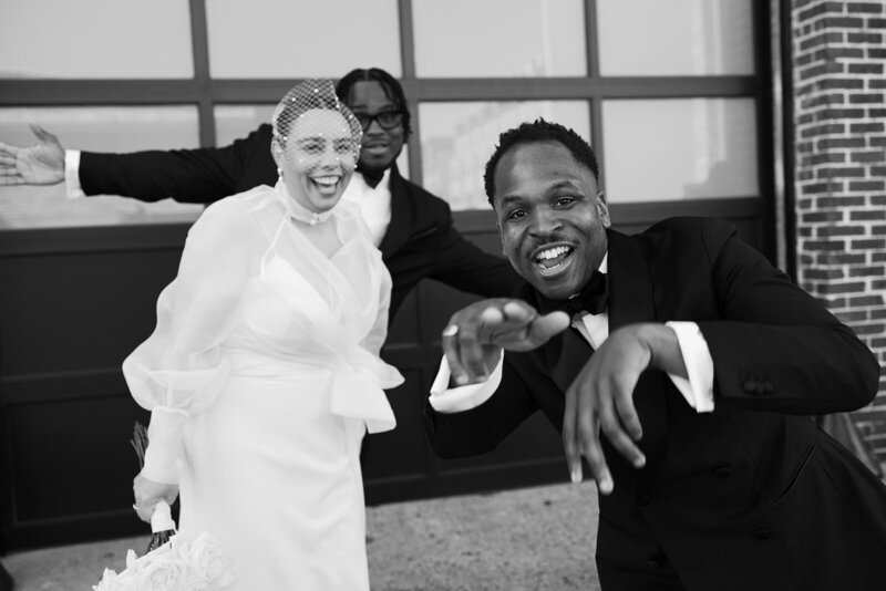 black and white photography of couple and groomsman pointing at camera laughing