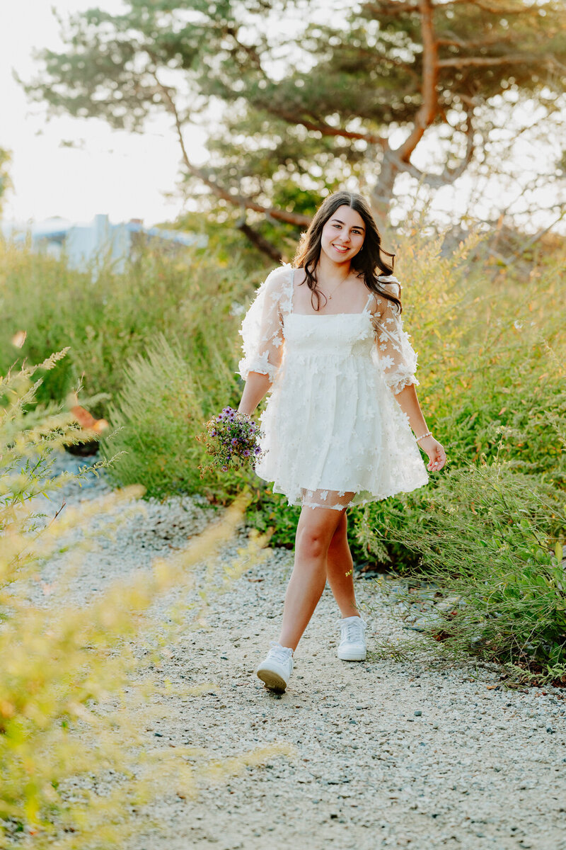 Girl wearing a white dress walking towards the camera for her senior pictures. 