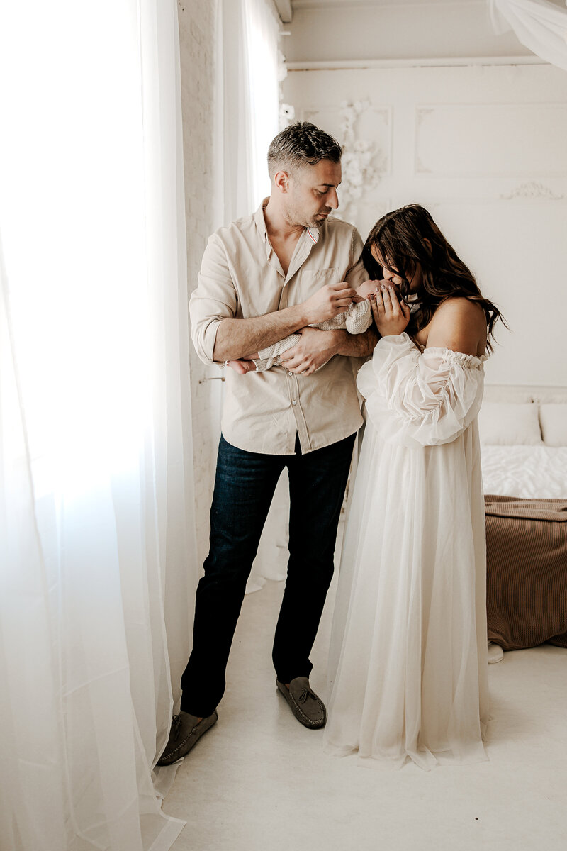 Elegant in-studio newborn photography session in South River, New Jersey featuring parents lovingly holding their baby in soft natural light.