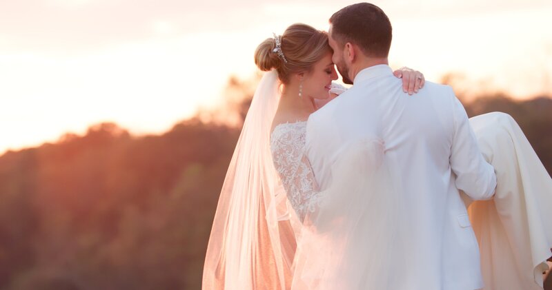 groom holding bride in arms with back to camera in golden hour