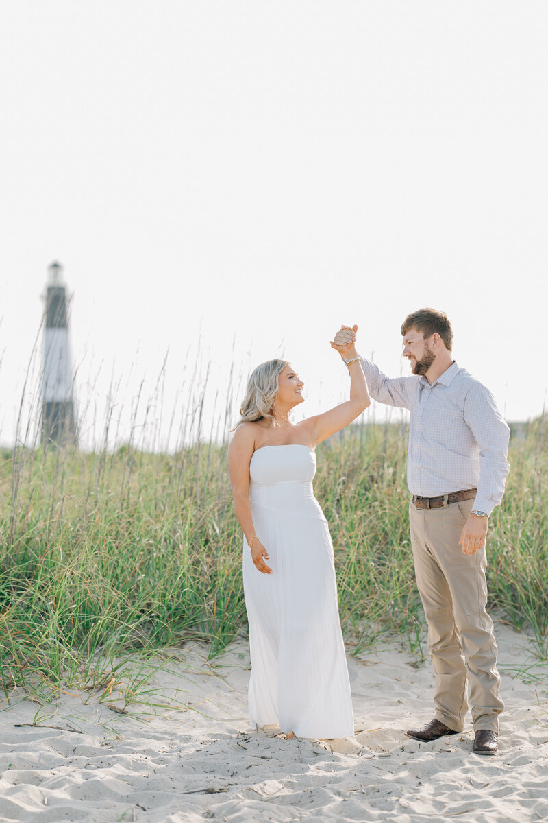 a couple dancing on the beach with a lighthouse in the distance