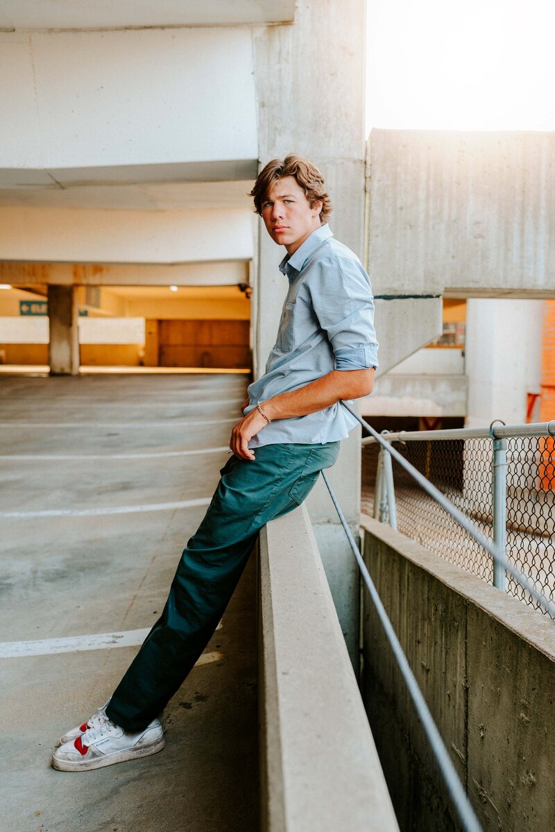 Senior boy leaning on a railing in a relaxed pose in a parking garage downtown Minneapolis, captured during a natural light senior photography session in the Twin Cities