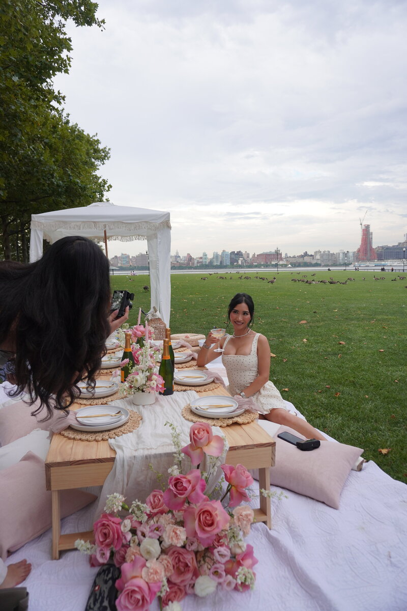 Luxury picnic setup with blush pink florals, elegant tableware, and city skyline views, styled by Yours Truly, a wedding planner and designer in New Jersey.