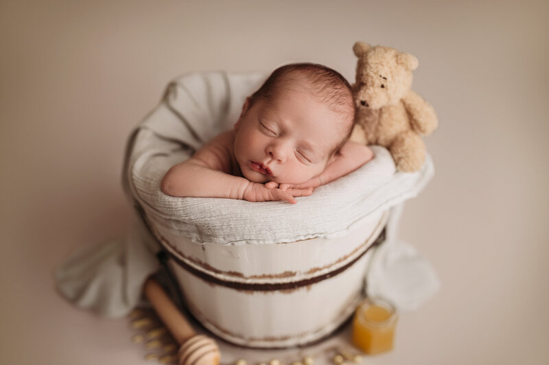 Newborn boy in a sleepy pose in white bucket with winnie the pooh and honey props
