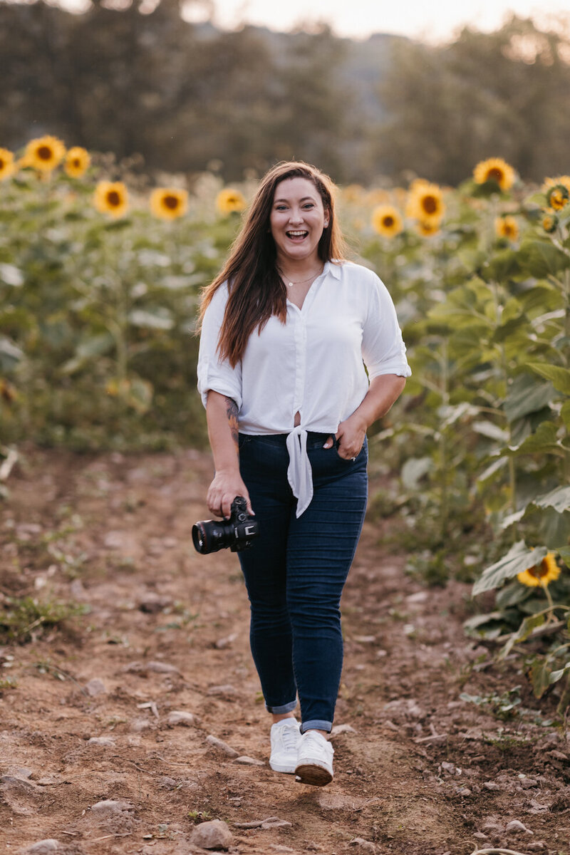 Nj engagement and wedding photographer, Melissa Lucas, poses in a sunflower field with her camera for her Blooming Faith Photography headshots