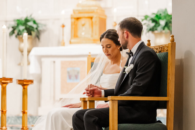 A bride and groom bow in prayer at the altar of a Catholic church, reflecting the sacredness of their union. This quiet, reverent moment honors the spiritual depth of a Christian wedding day. Captured by a North Texas photographer who values timeless imagery rooted in faith.