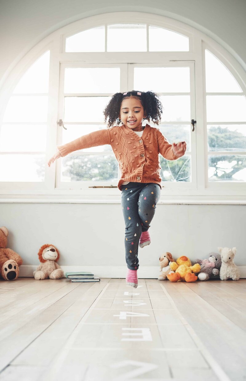 A young girl playing hopscotch indoors, practicing balance and coordination—highlighting how Pacific Kids Occupational Therapy supports early reflexes and movement foundations.