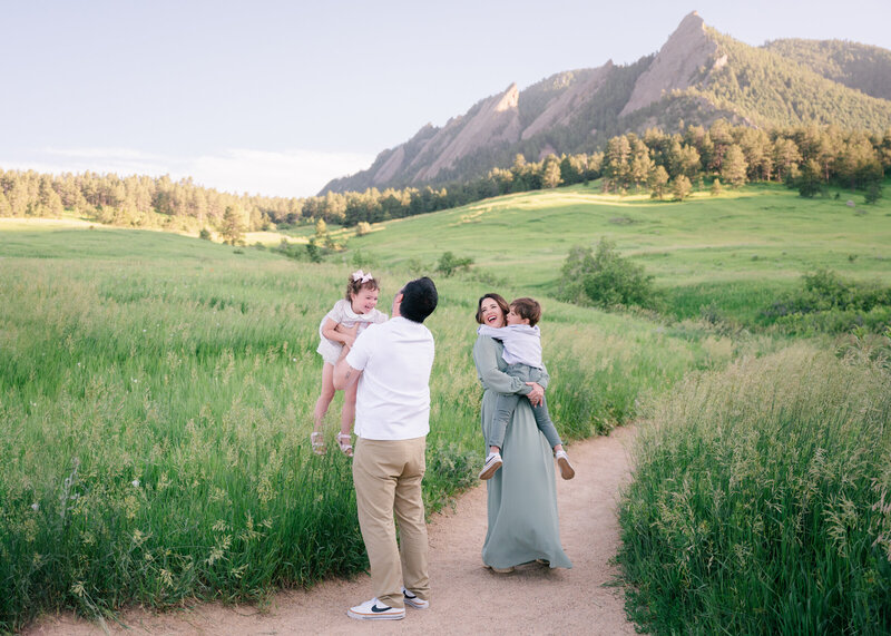 Family of 4 standing in front of the mountains wile they play with their small children- Maegan R Photography