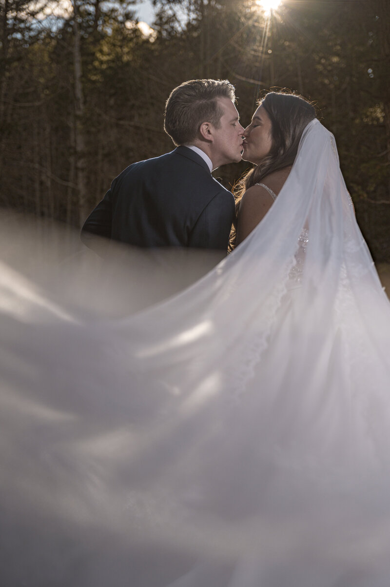 Bride and groom sharing a romantic kiss under a flowing veil at sunset — captured by Legacy in Light, Nebraska wedding photographer.