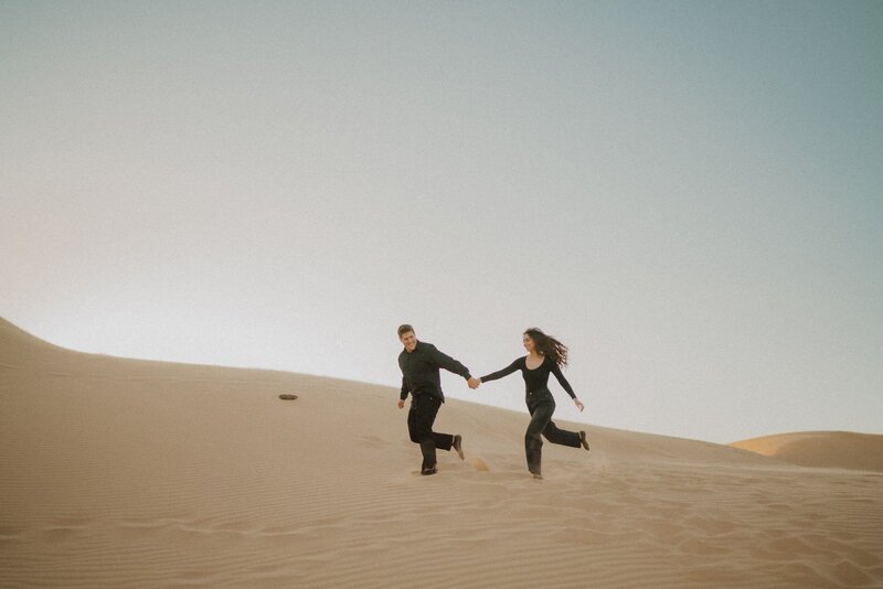 couple running through sand dunes