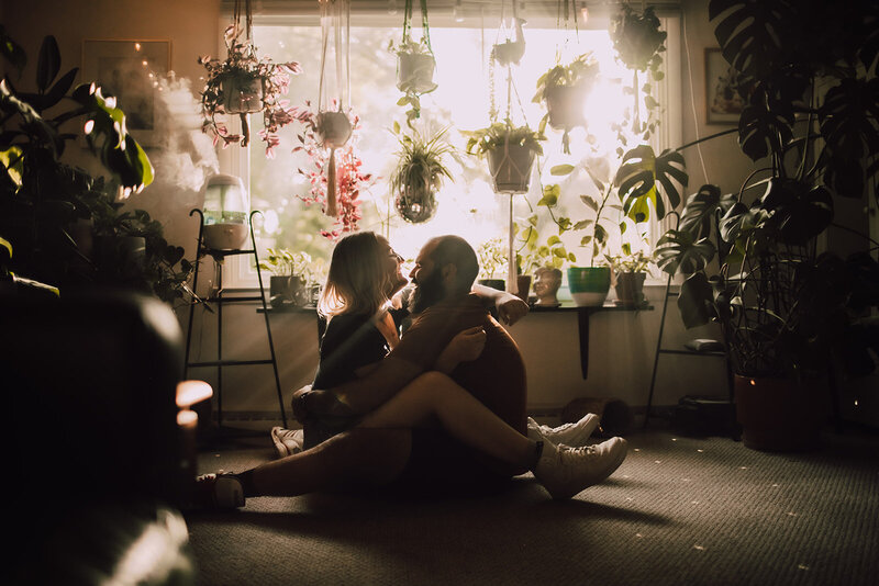 Man and woman sit in front of their plant lined apartment window