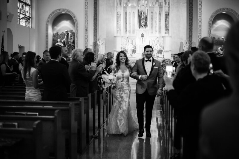 A timeless black-and-white moment from a wedding at Whitemarsh Valley Country Club in Lafayette Hill, PA, as the newlyweds walk down the aisle surrounded by family and friends.