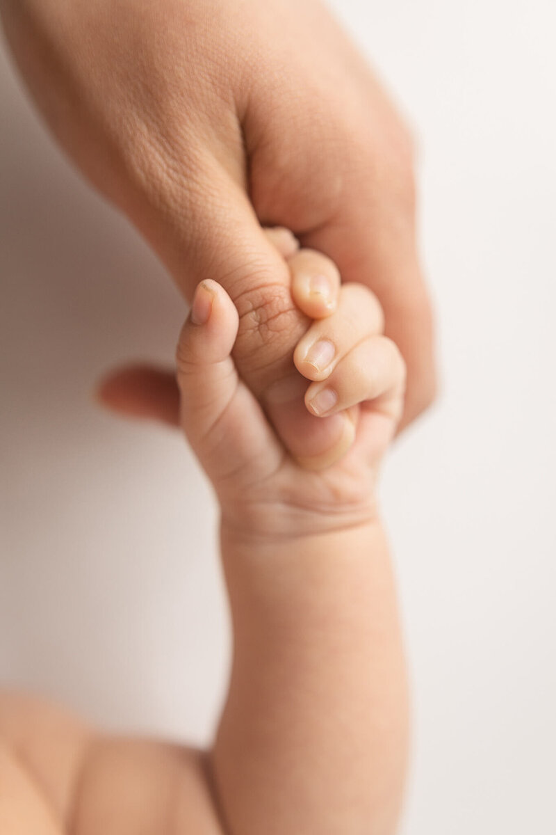 Tiny baby hand holding onto moms thumb.