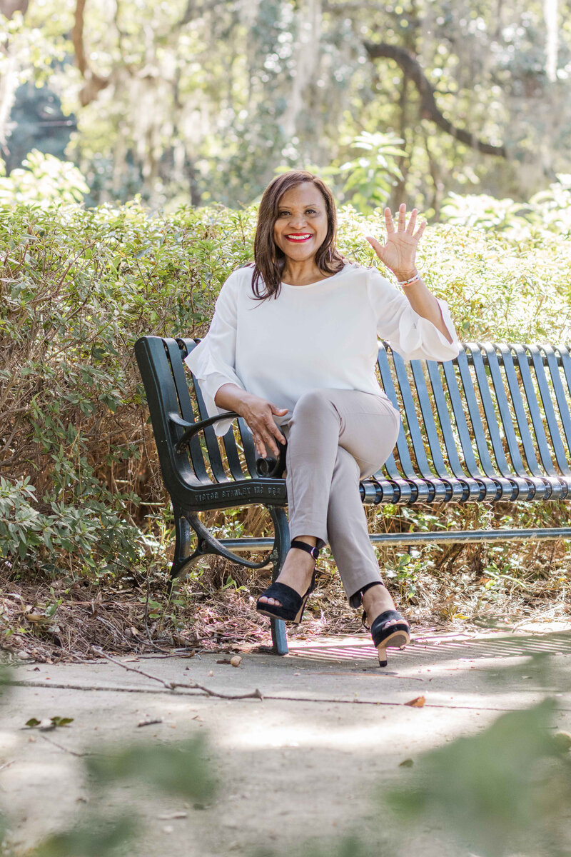 Sharon  Redman Health Coach sitting on a bench waving with her left hand