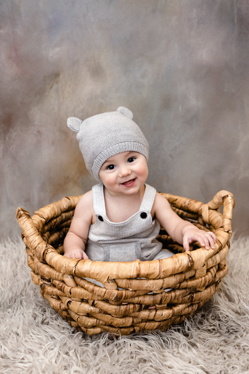 6 month old boy sitting in basket with cute teddy hat on