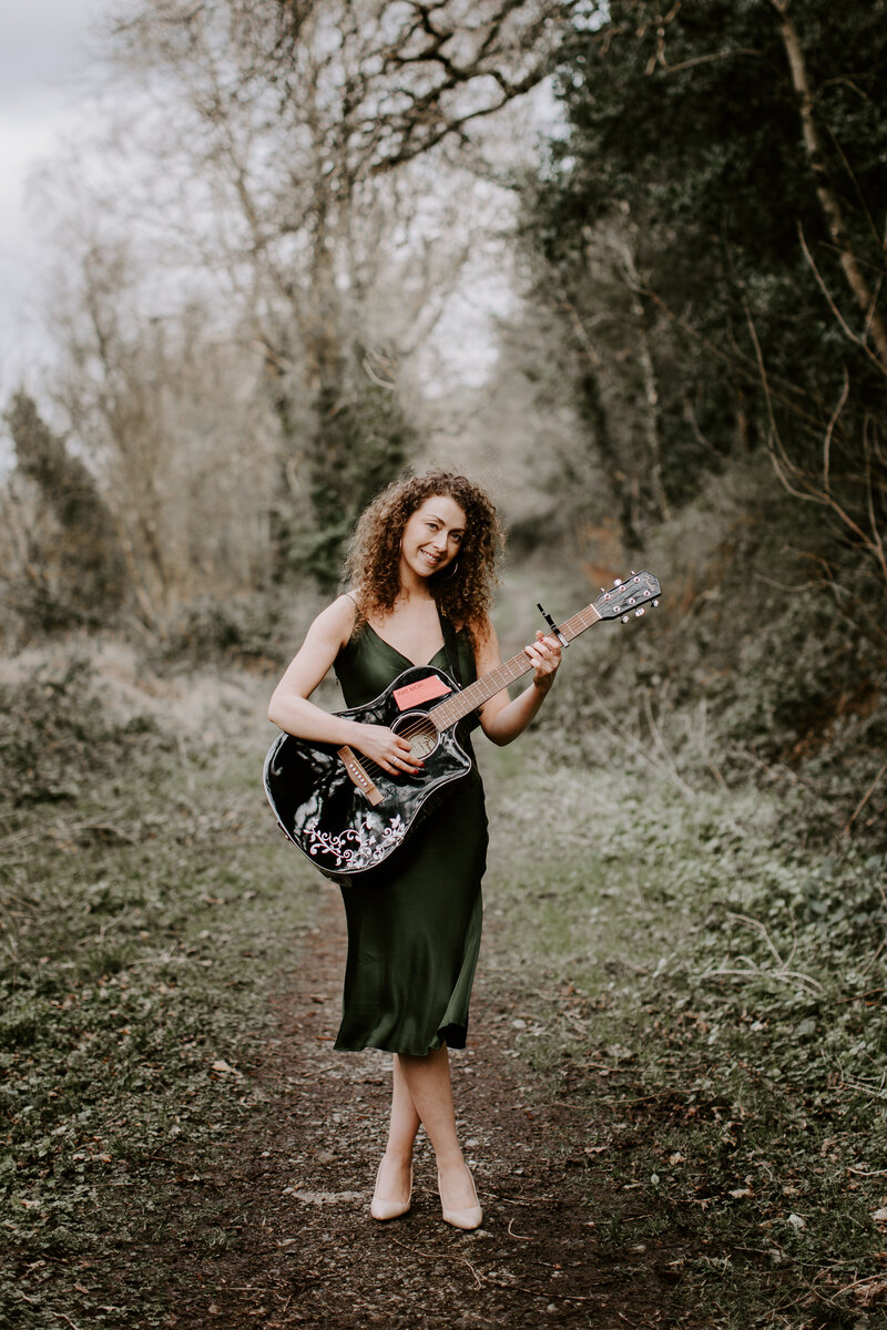 Seána Redmond smiling and holding a guitar, representing her musical journey from her No.1 hit “The Lonesome Boatman” to her performances with the Kilfenora Céilí Band and her work with the Global Citizen Award.