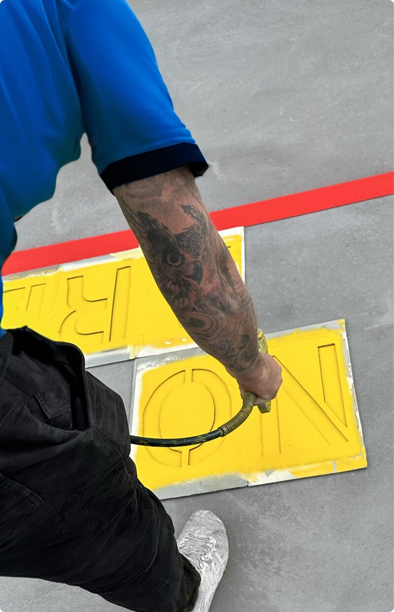 A Rapid Linemarking worker painting a yellow no parking wording on a concrete road.