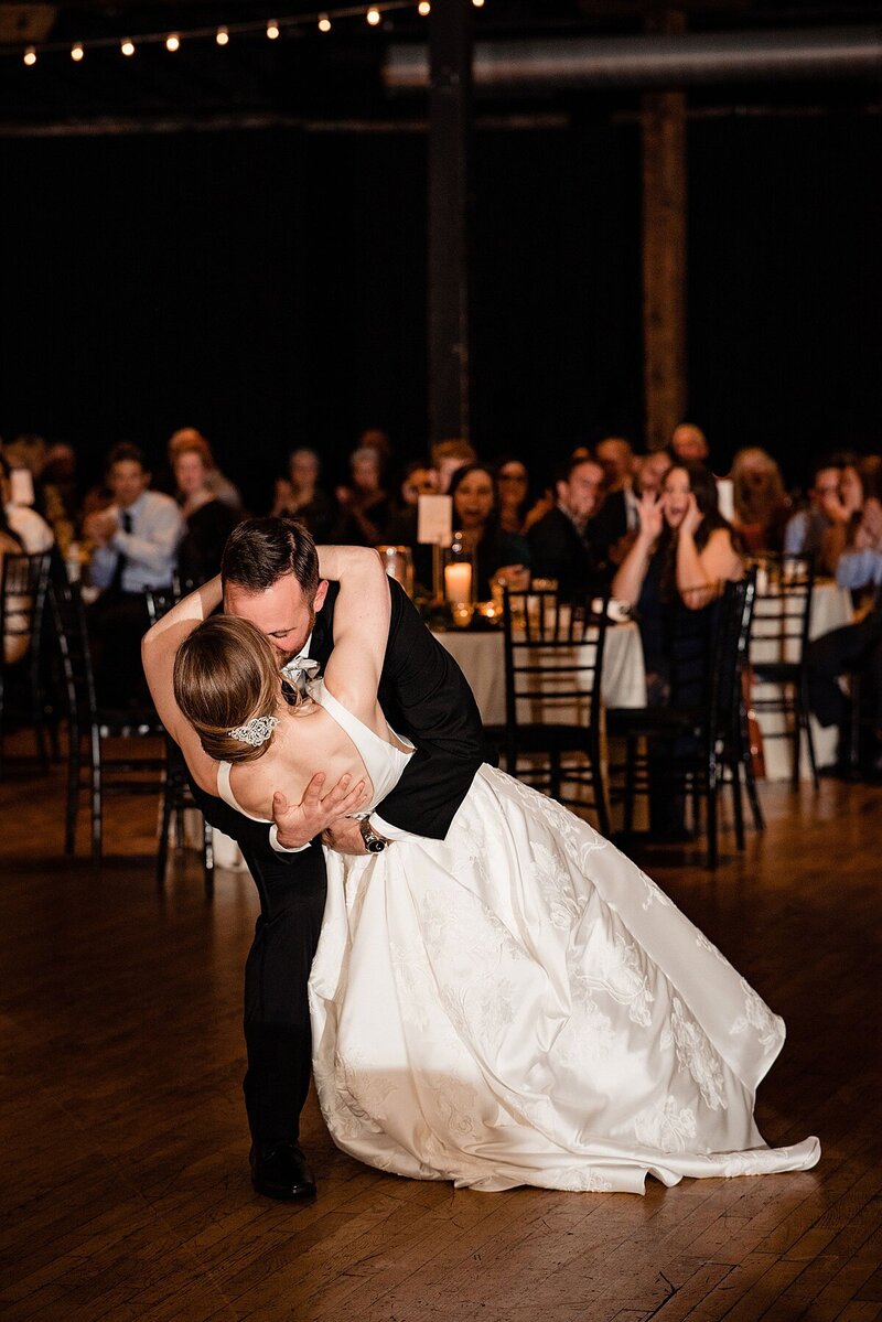 Groom dramatically dipping bride at the end of their first dance, guests are in the background clapping