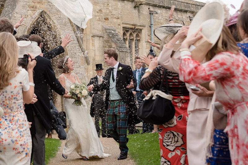 Bride and groom laughing as the bride's veil flies out while confetti is thrown
