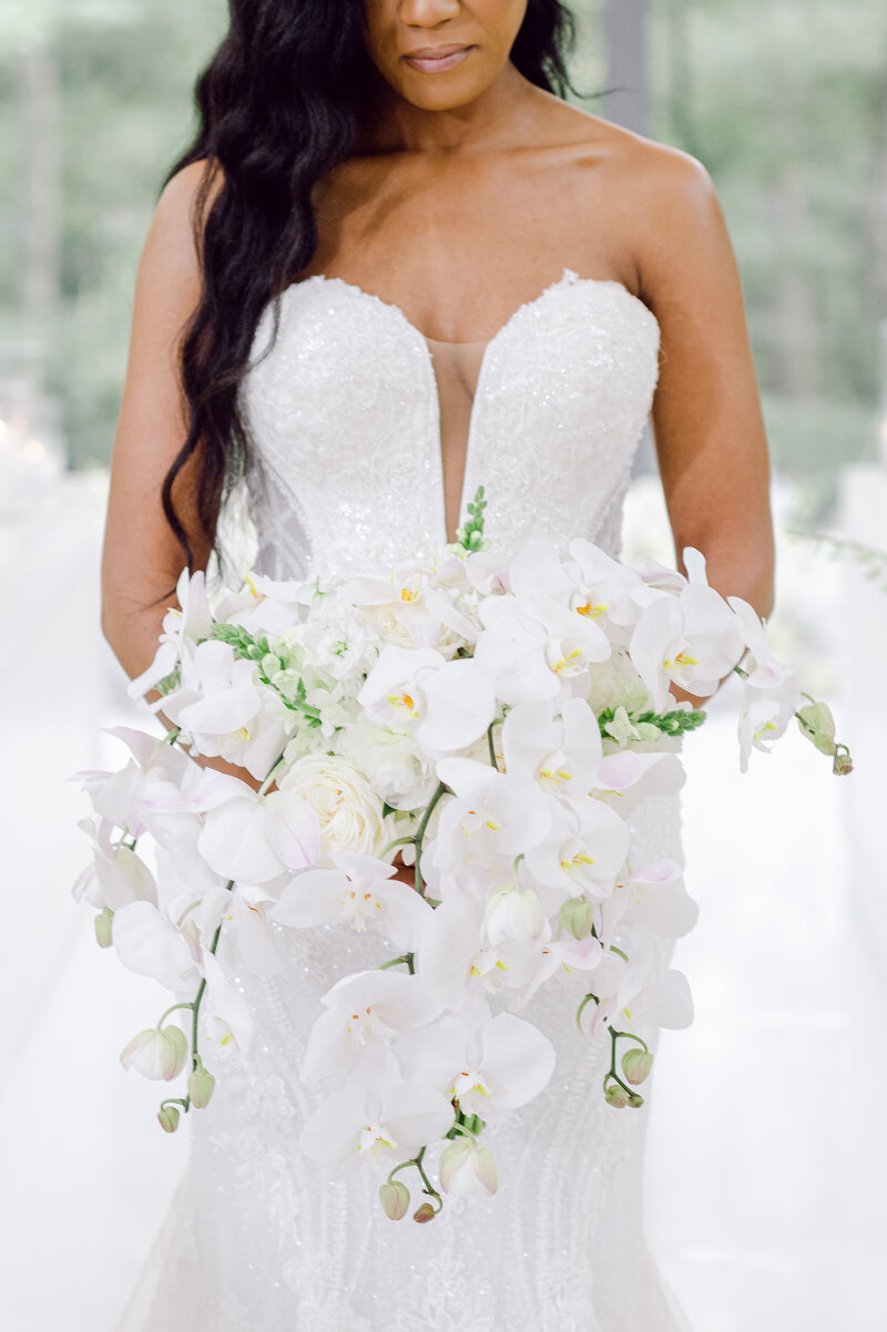 Bride in a strapless, beaded gown holding a cascading bouquet of white phalaenopsis orchids, roses, and snapdragons, designed by Wells Design Co.