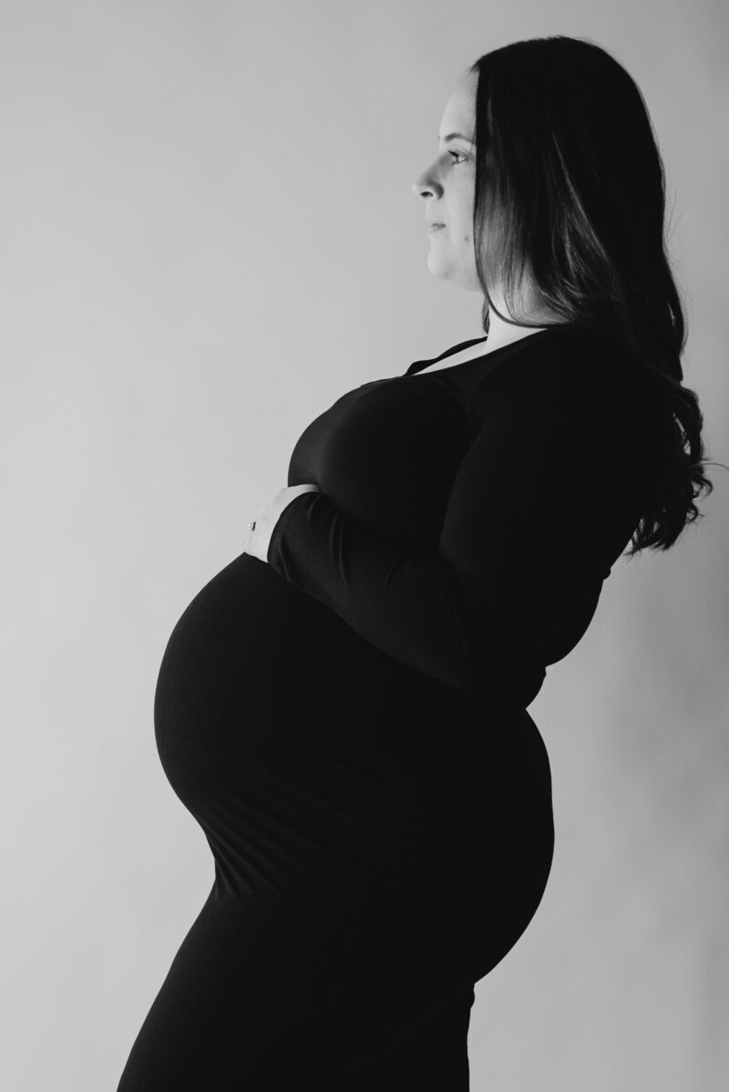 Black and white up close photo of moms pregnant belly in black dress with white background in studio in Annapolis Maryland.