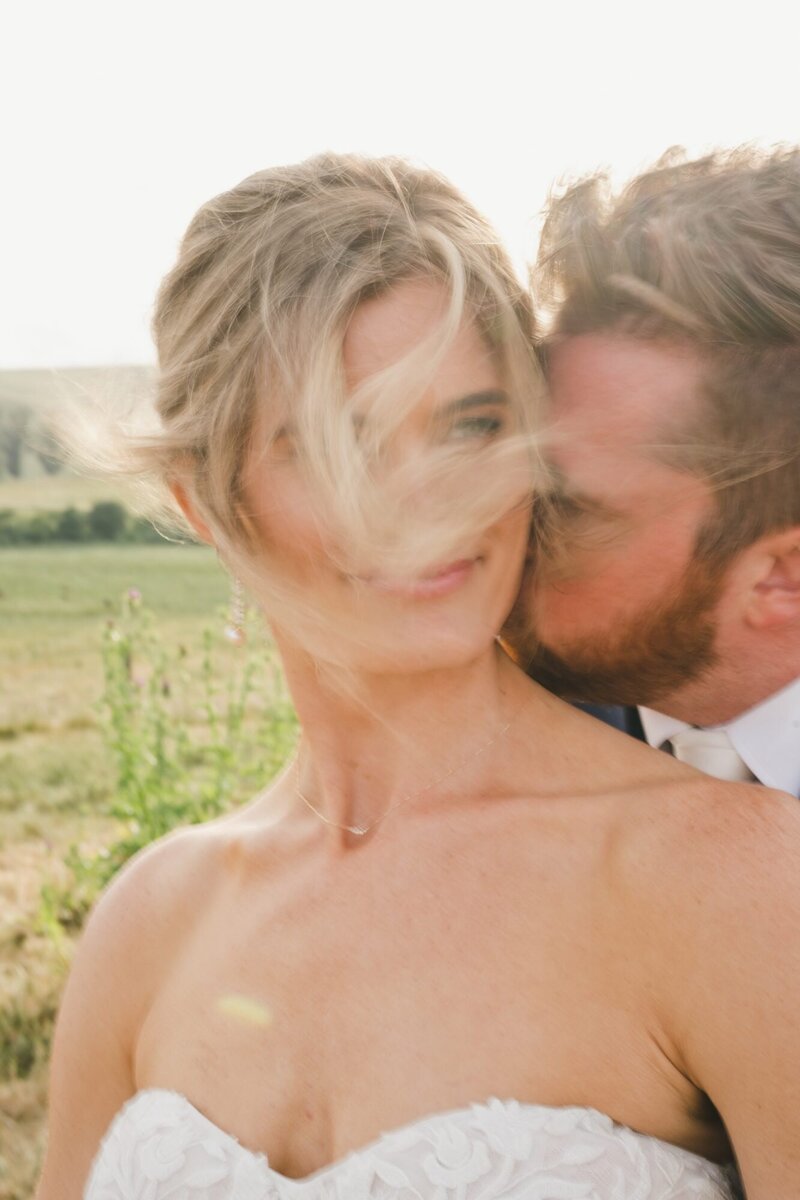 A candid wedding photo of a groom kissing his bridge on the cheek taken by One Love Photography.