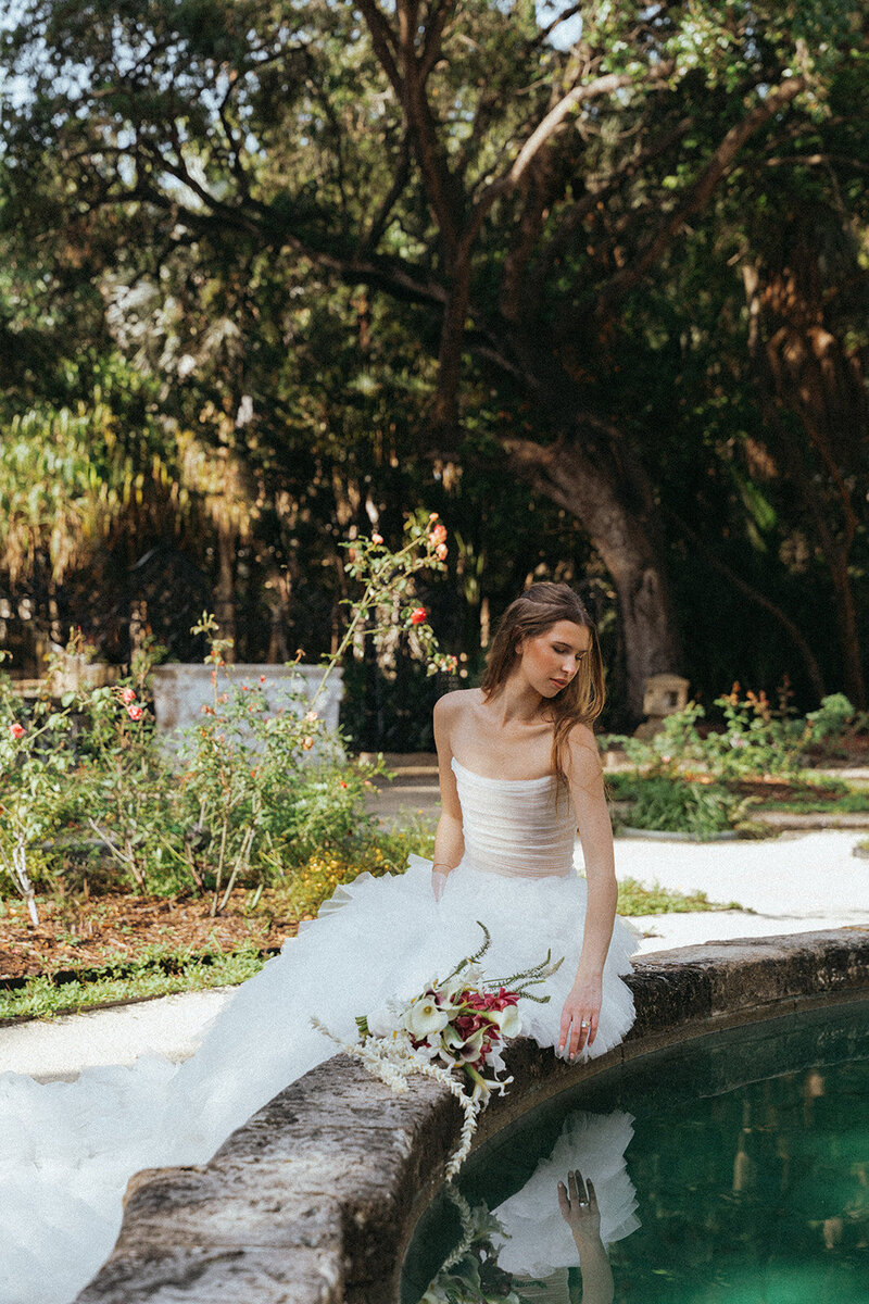 bride sitting by water with bouquet in miami wedding photos captured by elsie goodman, a destination and italy wedding photographer