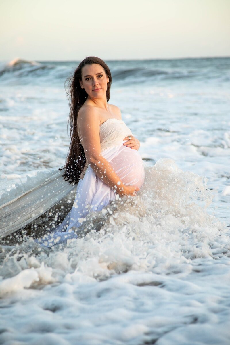 Christina standing in water holding her pregnant belly in Pacific Ocean | California Maternity Session
