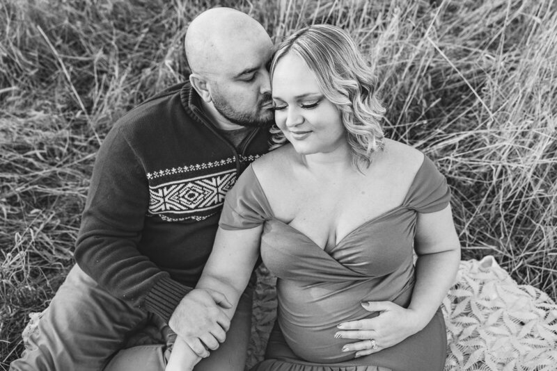 Black and white image of an expecting couple sitting in a field during winter in Farmington, Missouri. 