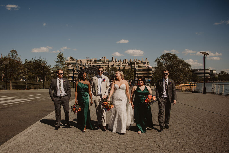 A newlywed couple walking with their wedding party down a sidewalk 