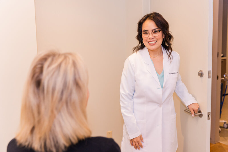 woman doctor plastic surgeon wearing white coat holding the door while entering a patient consultation brand photo Laure Photography