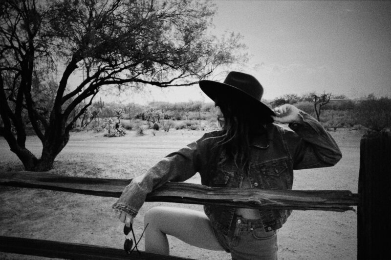 Black and white photo of a woman outdoors, showing her lower face, long braided hair, and off-the-shoulder top. The natural, blurry background evokes the artistry behind Sweet Pea Ink Creative’s unique brand design.