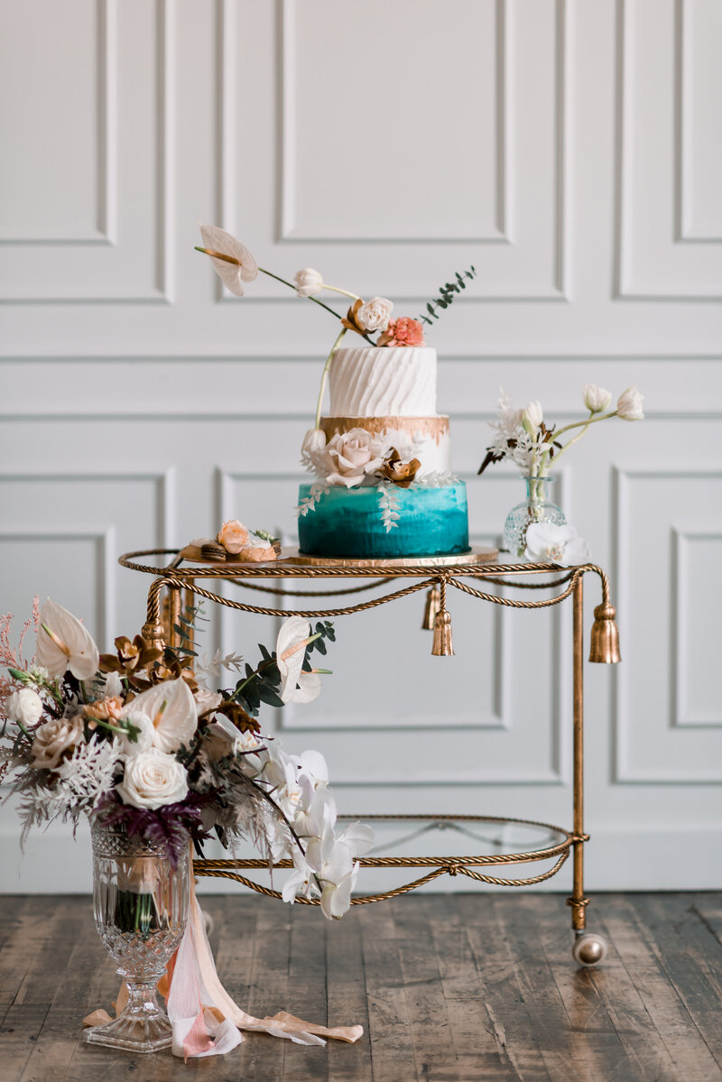 Beautiful wedding cake sits on gold cocktail cart