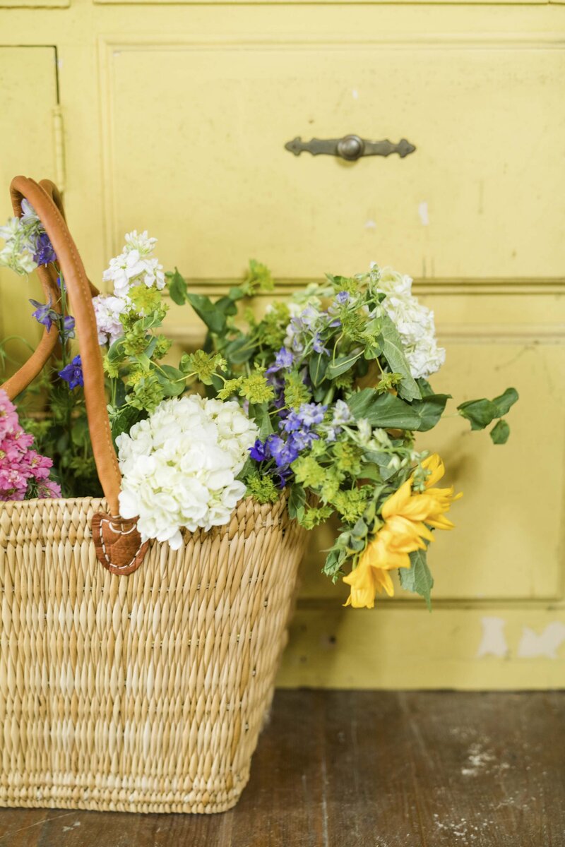 Bright flowers in basket rest against yellow wall