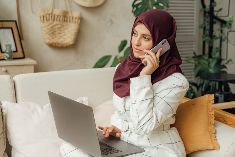 woman in hijab talking on the phone while sitting at her laptop - leo and vern