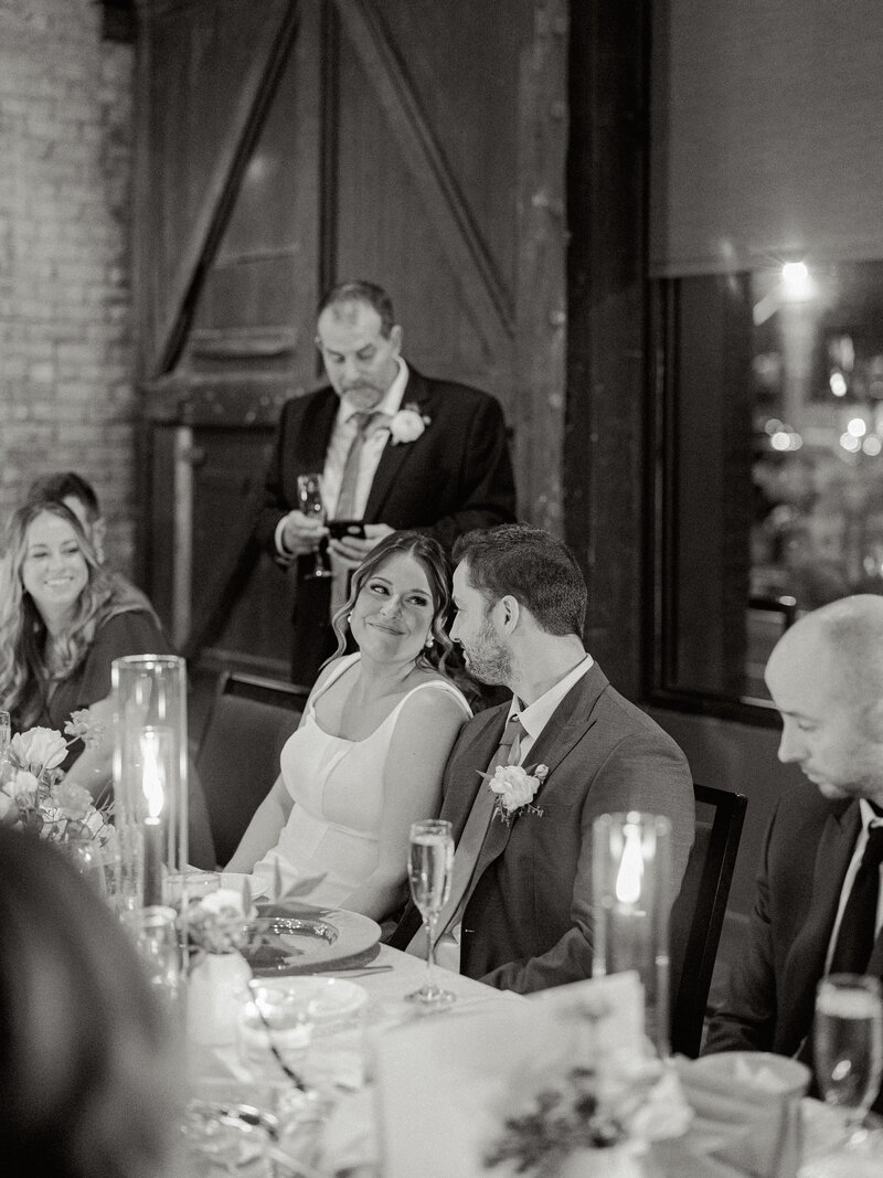 Black and white photo of the father of the bride toasting with the bride smiling at the groom and the groom looking back at her.
