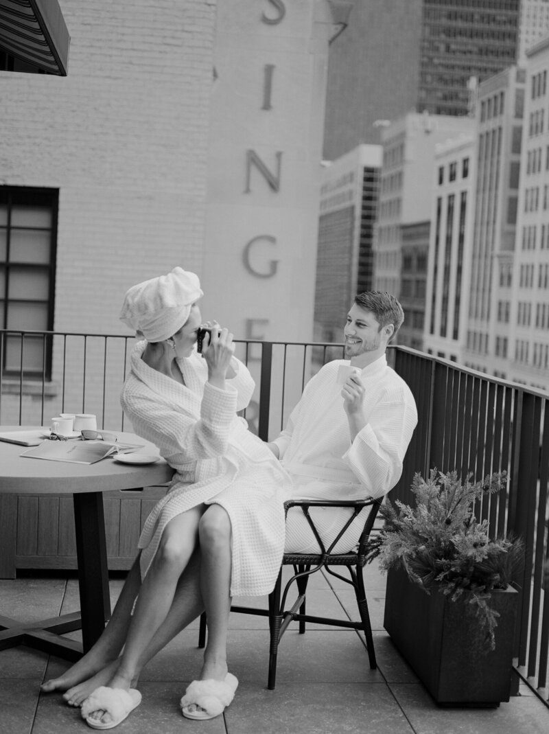 a couple photographs each other with an instant camera, bathrobes and coffee on the penthouse balcony of Shinola Hotel in Detroit, captured by film photographer Christina Harrison